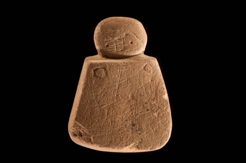 A photograph of a carved stone object shaped like a figure decorated with linear incisions